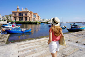 Young woman looking at Margherita Theater and fishing boats in the old harbor of Bari, region of Apulia, Italy