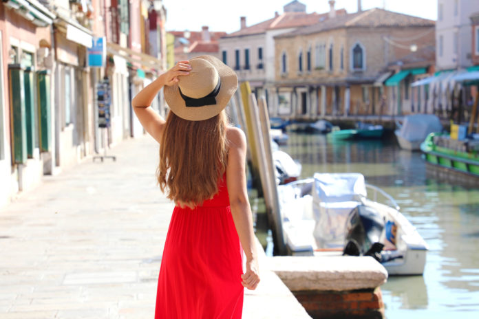 Beautiful slim model with red dress and hat walking in Murano, Venice