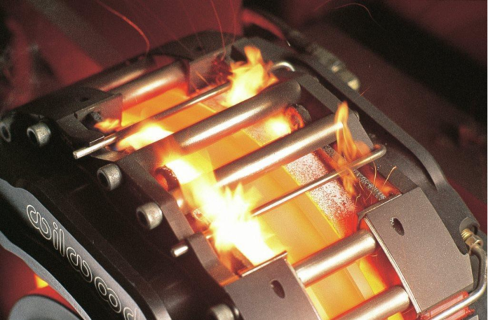 Dischi freno surriscaldati con pinza incandescente e fiamme visibili durante un test estremo di frenata